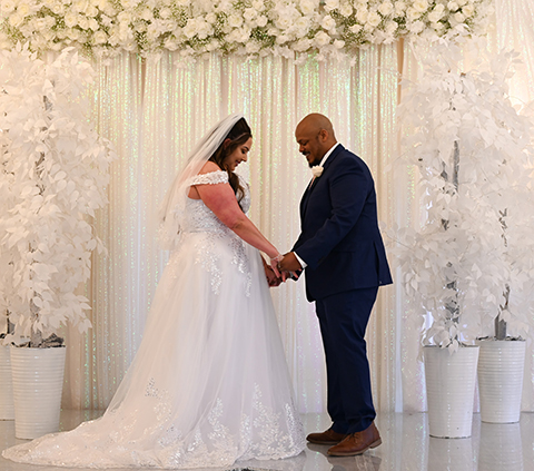A man and woman holding hands in front of white flowers.